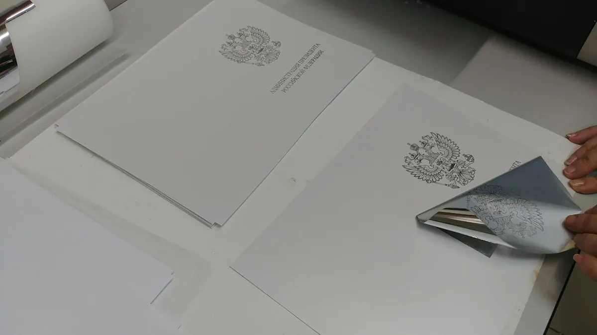 Снятие фольги с листа бумаги с отпечатанным гербом при фольгировании