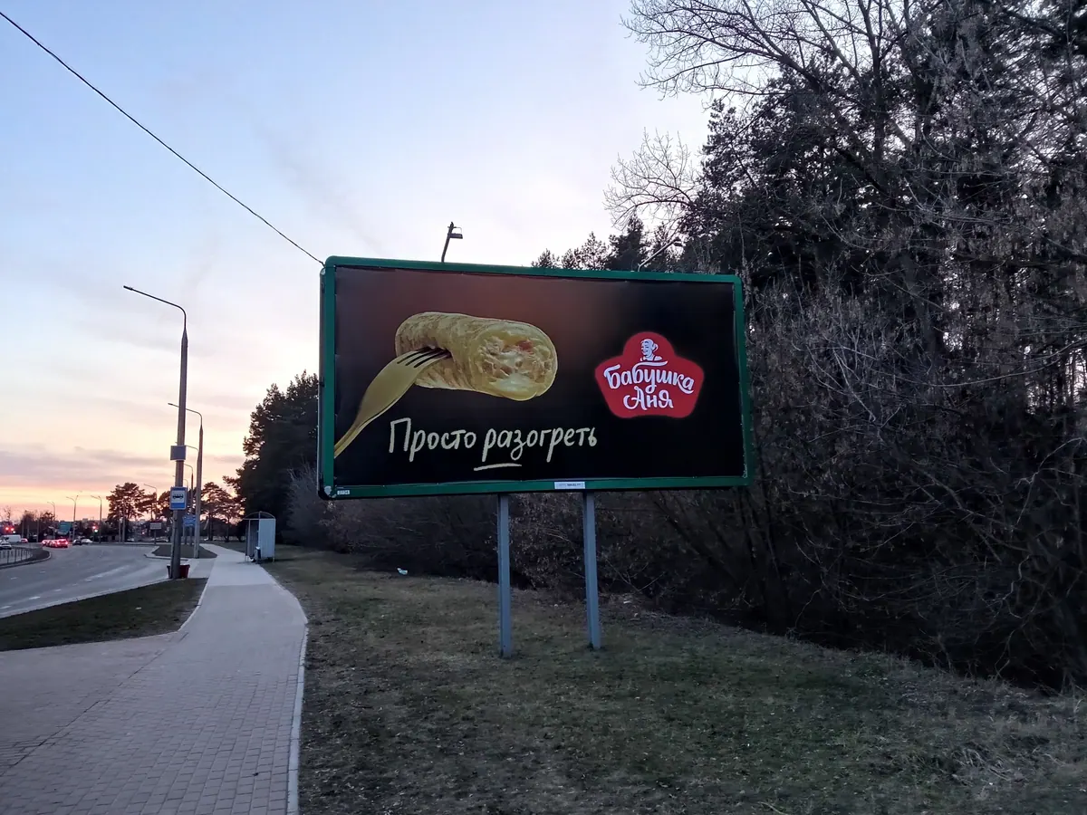 Рекламный билборд у дороги с надписью Просто разогреть и логотипом Бабушка Аня