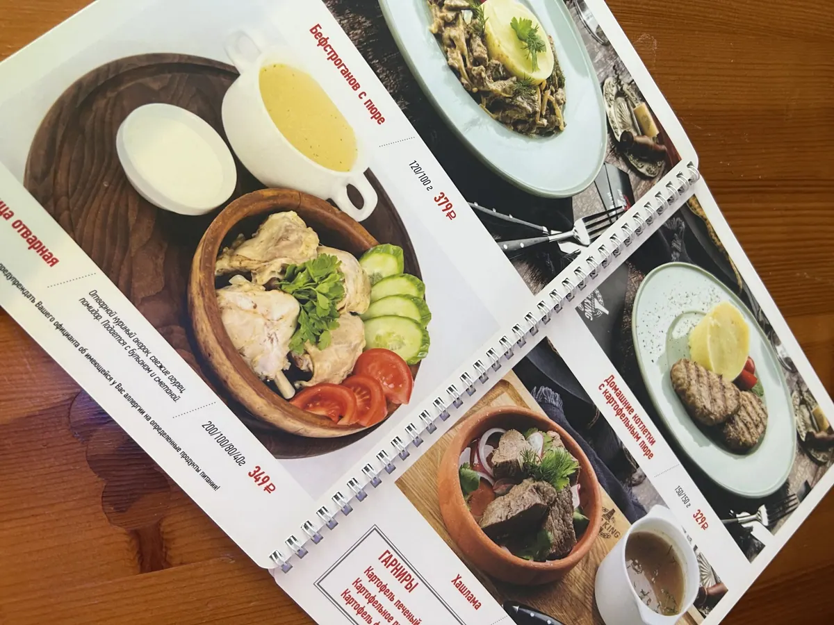 Раскрытое меню кафе на металлической пружине с фотографиями блюд и ценами