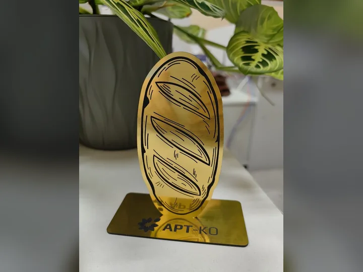Золотистая статуэтка в форме буханки хлеба с гравировкой на подставке