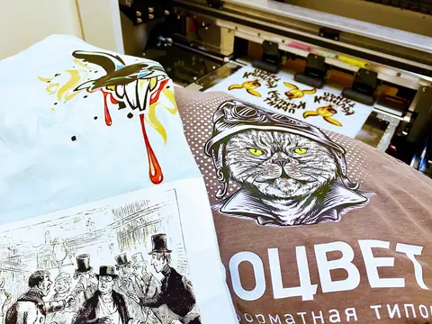 Образцы DTF-печати на футболках на фоне принтера с рулоном плёнки
